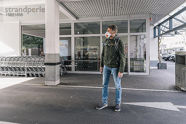 Mann mit Maske steht vor dem Supermarkt