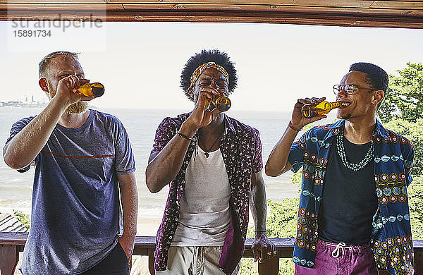 Multi-ethnische männliche Freunde trinken Bier  während sie auf dem Balkon stehen