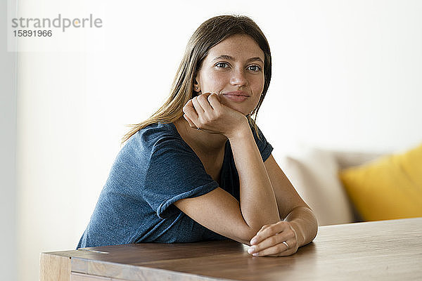 Porträt einer selbstbewussten jungen Frau  die zu Hause am Tisch sitzt