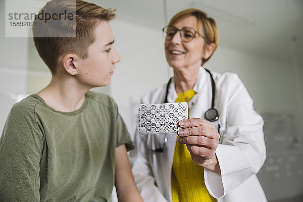 Arzt erklärt Teenager-Jungen in medizinischer Praxis Medikamente
