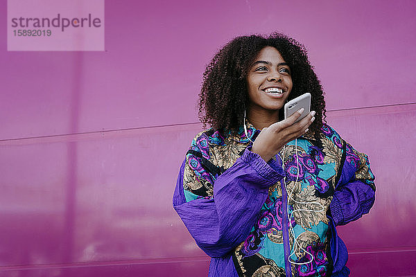 Lächelnde Frau benutzt Freisprechtelefon  rosa Wand im Hintergrund