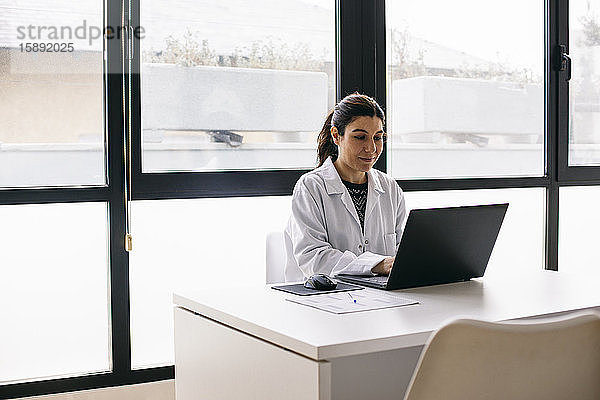 Arzt am Schreibtisch sitzend in medizinischer Praxis mit Laptop