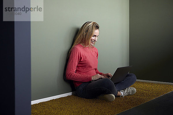 Lächelndes Womansitting auf dem Boden mit Laptop