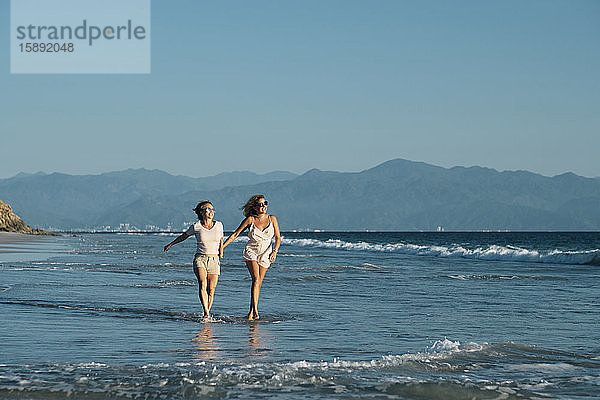 Sorglose reife Lesben in voller Länge  die am Strand am Strand bei strahlend blauem Himmel an der Riviera Nayarit  Mexiko  spazieren gehen