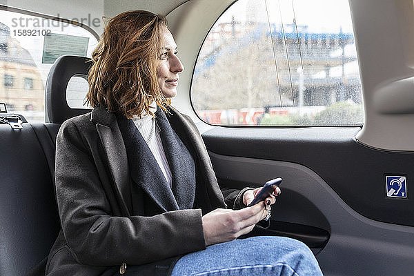 Geschäftsfrau auf dem Rücksitz eines Taxis  die aus dem Fenster schaut  London  UK