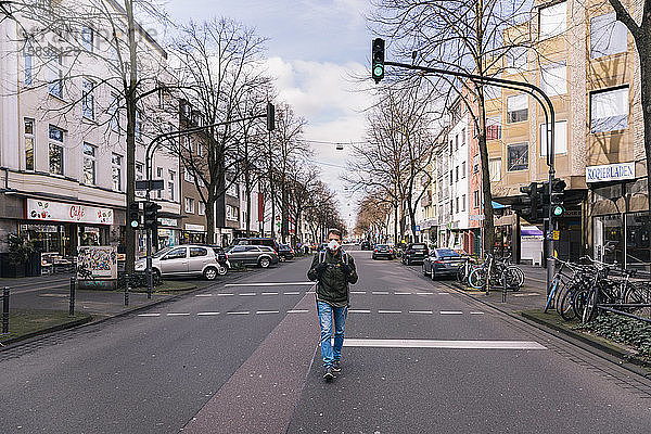 Mann mit Maske geht mitten auf einer leeren Straße in der Stadt