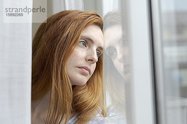 Porträt einer seriösen jungen Frau  die aus dem Fenster schaut