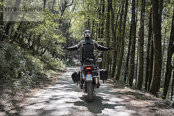 Motorradfahrer auf einer Fahrt auf einem Waldweg mit ausgestreckten Armen