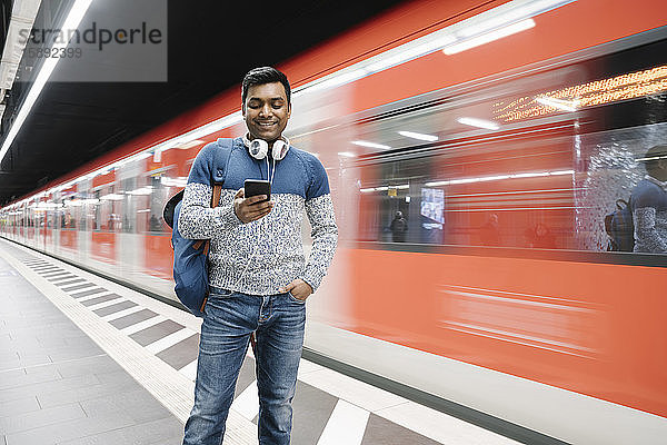 Lächelnder Mann benutzt Smartphone in U-Bahn-Station