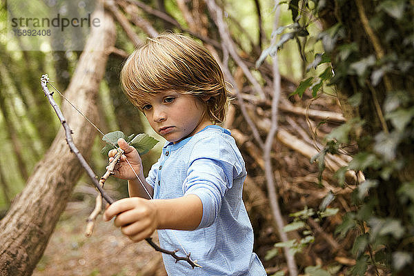Junge spielt mit Pfeil und Bogen im Wald