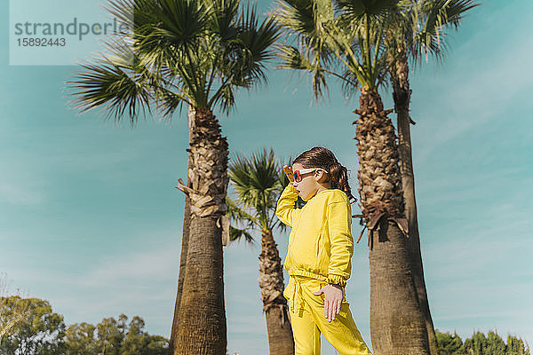 Kleines gelb gekleidetes Mädchen vor Palmen stehend