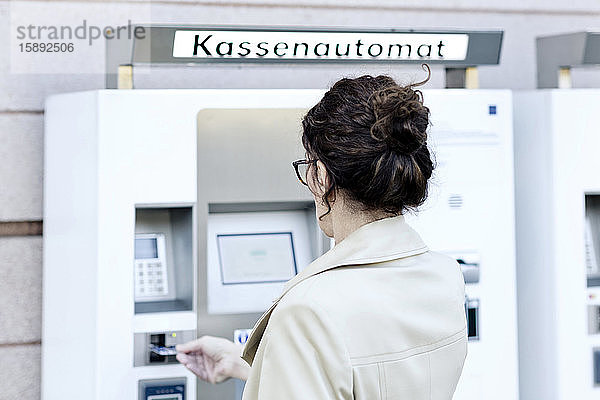 Rückansicht einer reifen Frau am Lohnautomaten