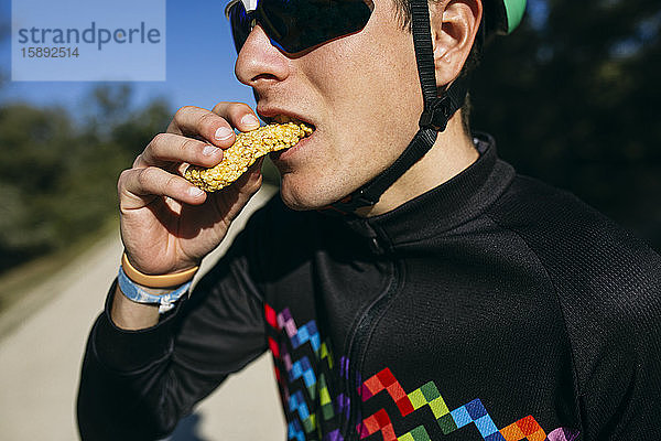 Porträt eines Radfahrers  der an einem sonnigen Tag in einer Pause eine Kleinigkeit isst