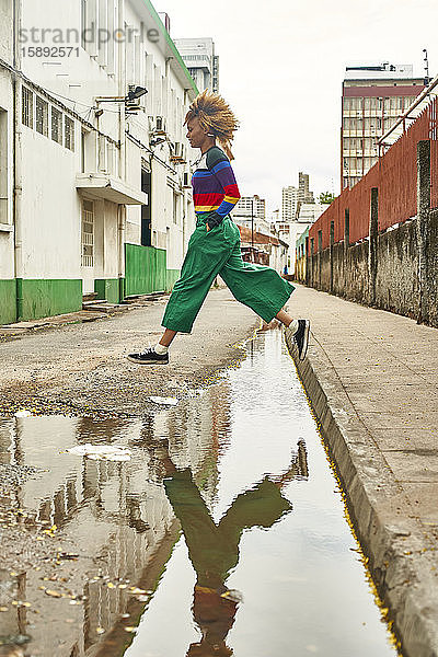 Junge Frau springt über Pfütze auf einer Straße