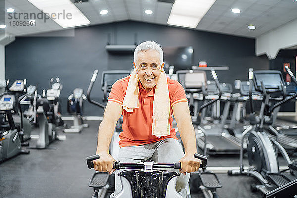 Porträt eines lächelnden älteren Mannes beim Üben an der Übungsmaschine im Fitnessstudio