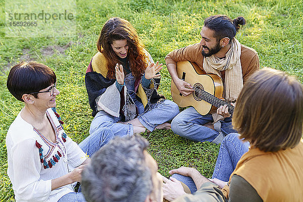 Gruppe von Freunden  die mit der Gitarre musizieren und auf dem Rasen im Feld sitzen
