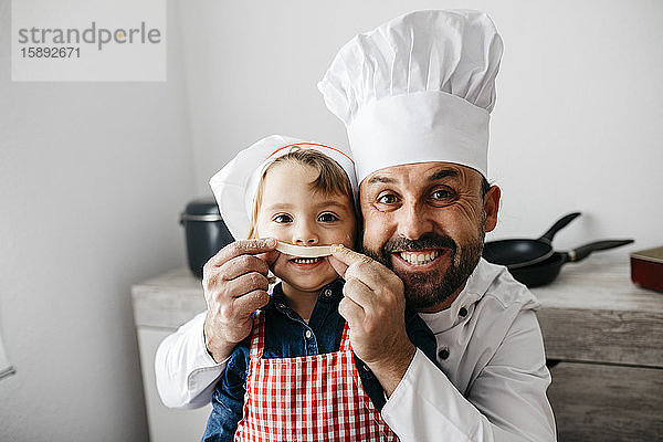 Verspielter Vater mit Tochter amüsiert sich beim Zubereiten selbstgemachter Pasta in der heimischen Küche