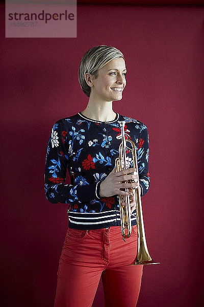 Lächelnde blonde Frau mit einer Trompete in der Hand