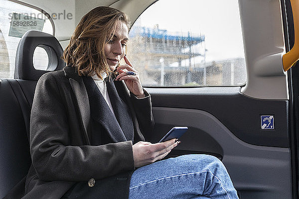 Geschäftsfrau auf dem Rücksitz eines Taxis mit Blick auf das Telefon