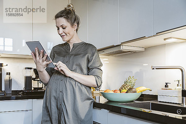 Schwangere Frau benutzt Tablette in der Küche zu Hause
