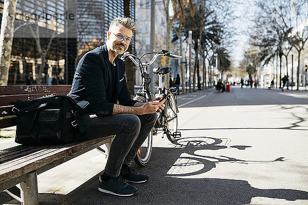 Porträt eines grauhaarigen Geschäftsmannes  der in der Stadt auf einer Bank neben dem Fahrrad sitzt