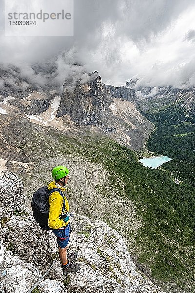 Junger Mann  Bergsteiger an einem Klettersteig  Via Ferrata Vandelli  Blick auf Lago di Sorapis  Sorapiss Umrundung  Berge mit tiefhängenden Wolken  Dolomiten  Belluno  Italien  Europa
