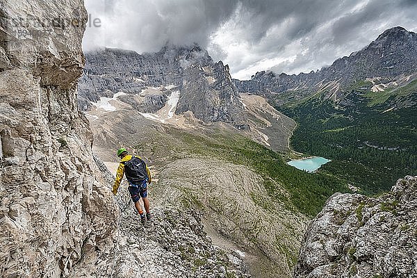 Junger Mann  Wanderer an einem Klettersteig  Via Ferrata Vandelli  Blick auf Lago di Sorapis  Sorapiss Umrundung  Berge mit tiefhängenden Wolken  Dolomiten  Belluno  Italien  Europa