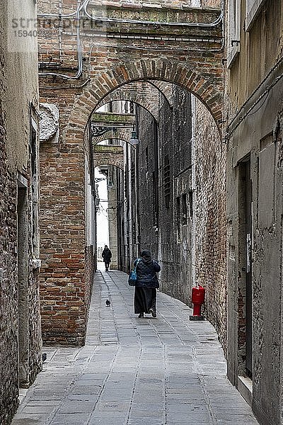 Frau mit Kopftuch und Tasche in einer schmalen Gasse  Hochformat  Venedig  Venetien  Italien  Europa