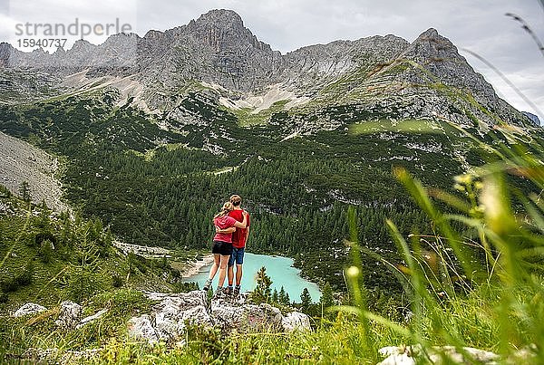 Beim Wandern  junger Mann und junge Frau  Paar steht auf Stein mit Blick auf türkisgrünen Sorapiss See und Berglandschaft  Dolomiten  Belluno  Italien  Europa