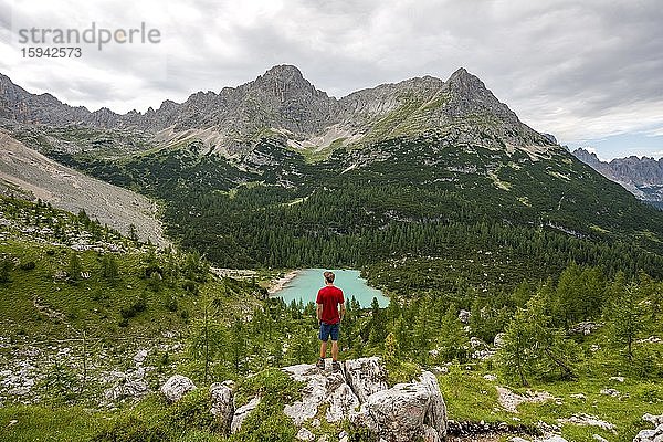 Junger Mann  Wanderer steht auf Felsen und blickt auf türkisgrünen Sorapiss See und Berglandschaft  Dolomiten  Belluno  Italien  Europa