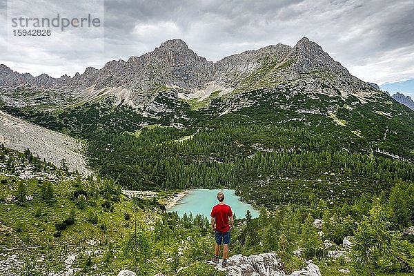 Junger Mann  Wanderer steht auf Felsen und blickt auf türkisgrünen Sorapiss See und Berglandschaft  Dolomiten  Belluno  Italien  Europa