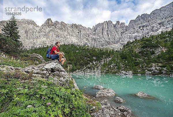 Wanderer sitzt  rastet auf einem Fels an türkisgrünem Sorapissee  Lago di Sorapis  Dolomiten  Belluno  Italien  Europa