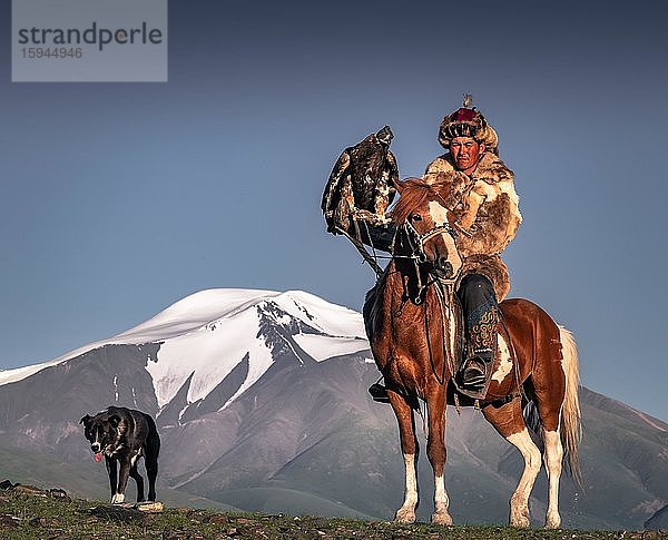 Mongolischer Adlerjäger  Kasachisch zu Pferd mit dressiertem Adler vor schneebedeckten Bergen  Provinz Bajan-Ölgii  Mongolei  Asien