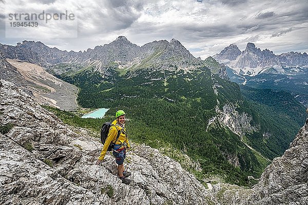 Junger Mann  Wanderer an einem Klettersteig  Via Ferrata Vandelli  Blick auf Lago di Sorapis und Berggipfel Cime de Laudo und Monte Cristallo  Sorapiss Umrundung  Berge mit tiefhängenden Wolken  Dolomiten  Belluno  Italien  Europa