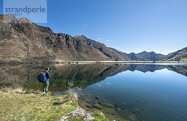 Wanderer steht an einem See  Berge spiegeln sich im See  Moke Lake bei Queenstown  Otago  Südinsel  Neuseeland  Ozeanien