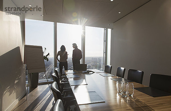 Geschäftsleute unterhalten sich am Fenster eines sonnigen Hochhaus-Konferenzraums