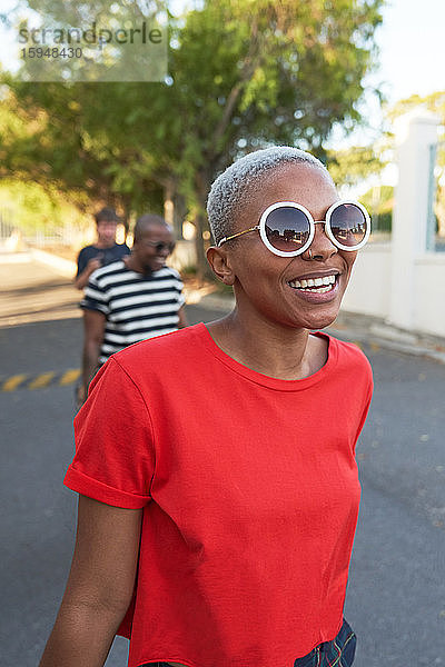 Glückliche junge Frau mit Sonnenbrille geht auf der Straße