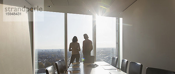 Geschäftsleute stehen am Fenster eines sonnigen Hochhaus-Konferenzraums