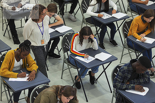 Gymnasiallehrer beaufsichtigt Schüler  die an Tischen Prüfungen ablegen