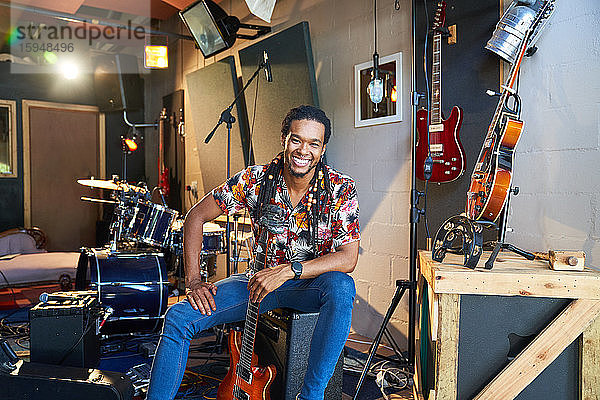 Porträt eines glücklichen  selbstbewussten männlichen Musikers mit Gitarre im Aufnahmestudio