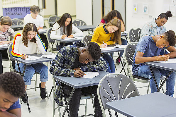 Fokussierte Gymnasiasten  die an Schreibtischen im Klassenzimmer Prüfungen ablegen