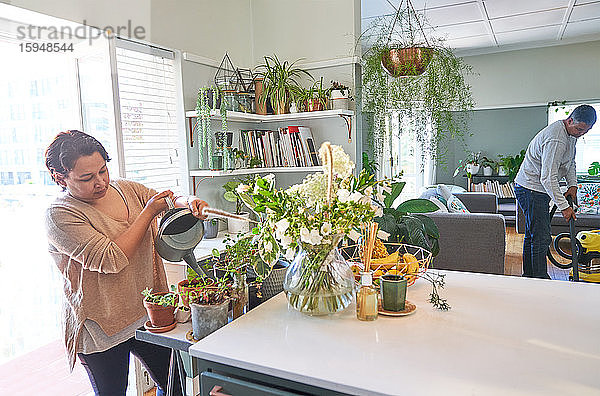 Reife Frau bewässert Zimmerpflanzen in der Küche