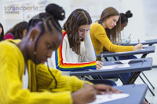 Fokussierte High-School-Schülerinnen  die ihre Prüfung am Schreibtisch im Klassenzimmer ablegen