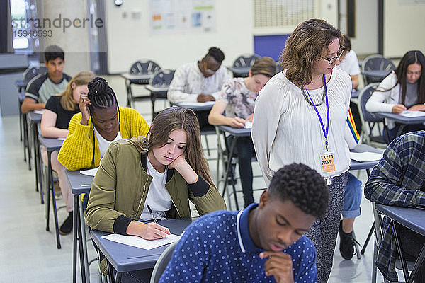 Gymnasiallehrer beaufsichtigt Schüler  die am Prüfungspult im Klassenzimmer sitzen