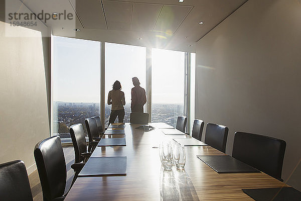 Geschäftsleute unterhalten sich am Fenster eines sonnigen Hochhaus-Konferenzraums