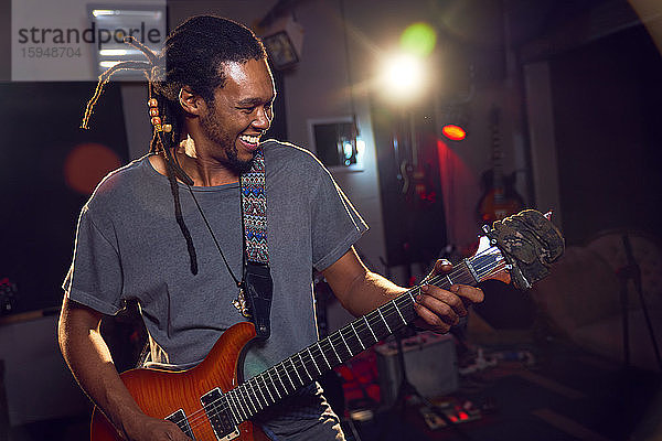 Glücklicher männlicher Musiker spielt E-Gitarre im Aufnahmestudio