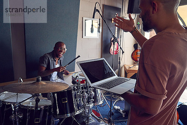 Glückliche Musiker mit Schlagzeug und Laptop im Aufnahmestudio