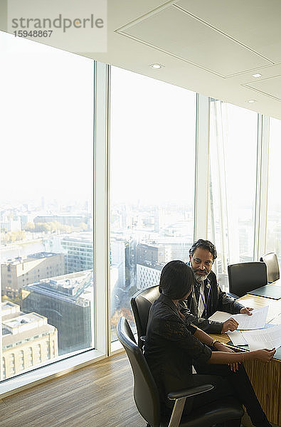 Geschäftsleute besprechen Papierkram in hochgelegenem Konferenzraum