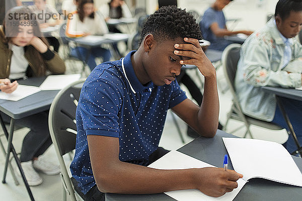 Fokussierter High-School-Junge nimmt Prüfung am Schreibtisch im Klassenzimmer ab