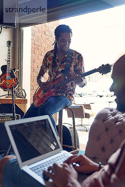 Männliche Musiker mit Laptop und Gitarre beim Üben im Aufnahmestudio
